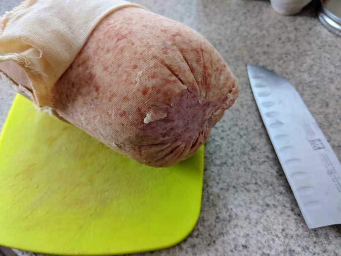 Buy in Bulk - Case Pork Roll Wrapped in Cheesecloth on a Cutting Board with a Knife
